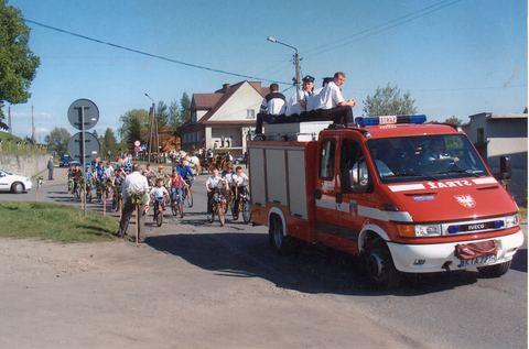 Samochód pożarniczy Iveco na ulicy wsi podczas rajdu rowerowego, wokół rowerzyści i mieszkańcy