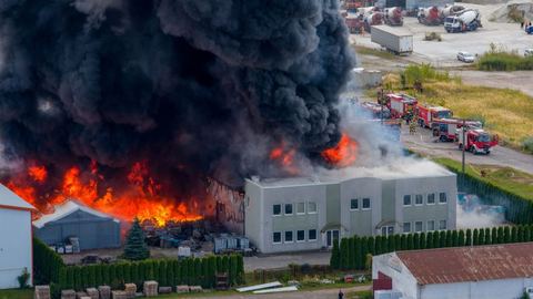 Widok z góry na pożar hurtowni zniczy: płomienie, czarny dym i wozy strażackie