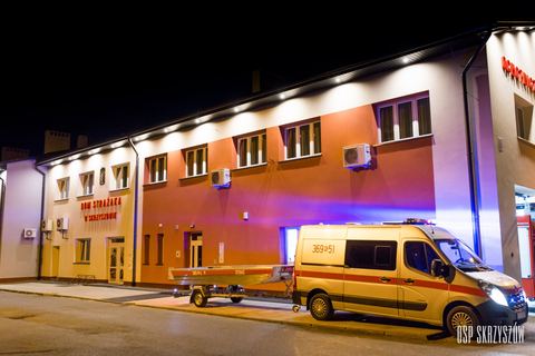 Samochód Renault Master z przyczepą i łodzią płaskodenną przed oświetlonym Domem Strażaka wieczorem